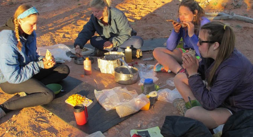 Four people sit on the ground while cooking and eating.